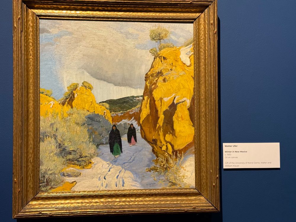 Painting of two women walking in snow against red rock boulders, in the Harwood Museum of Art, Taos NM