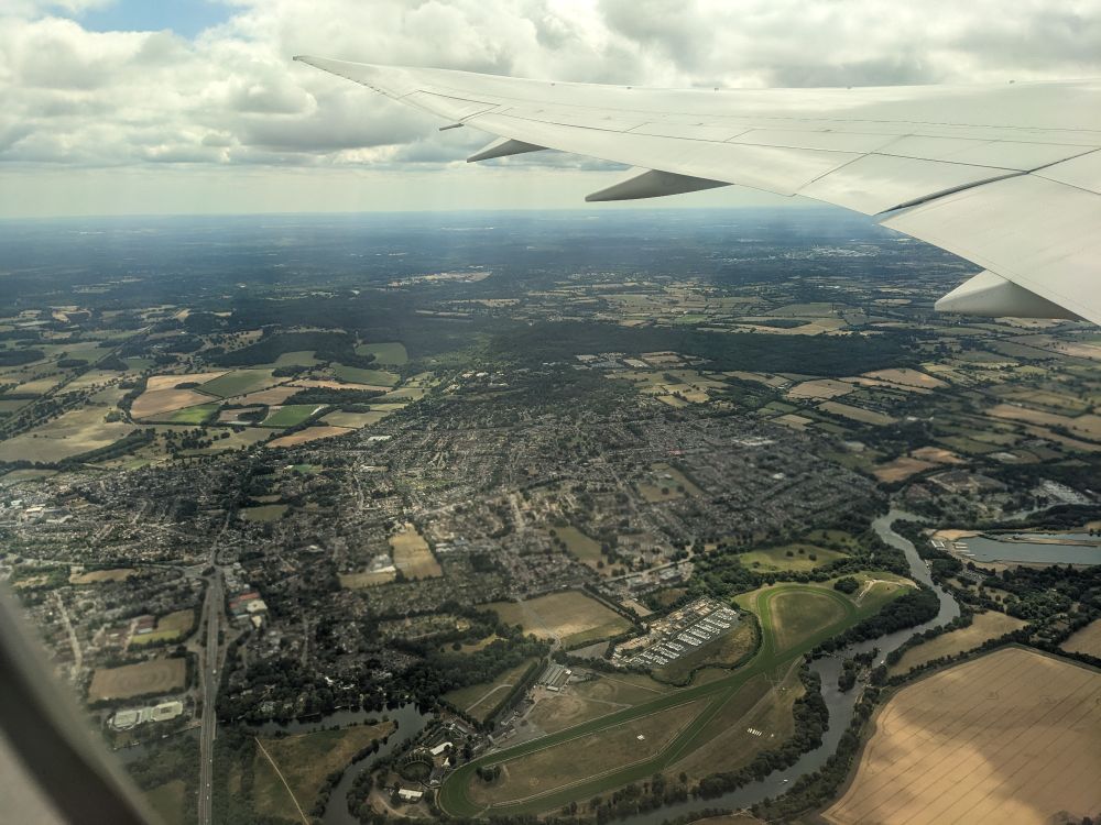 The view of the wing of an airplane out the window, with a view of the area around London, UK spread out below.