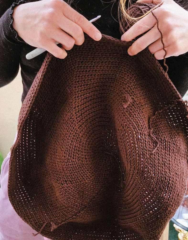 Nahaufnahme eines gehäkelten, braunen Kreises aus dicker Wolle. Das rund gearbeitete Stück liegt auf einem hellen Hintergrund, ist gleichmäßig gearbeitet und deutet bereits eine halbkugelige Form an