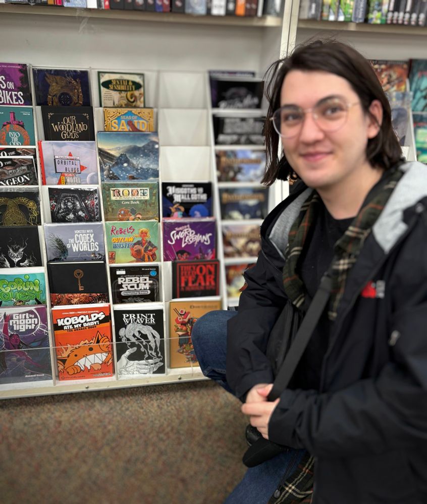nl sitting in front of a book store shelf, proudly displaying print weaver (a game they wrote)