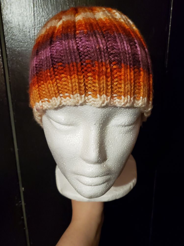 Photo of a foam head wearing a knit ribbed beanie in the colors of the lesbian pride flag