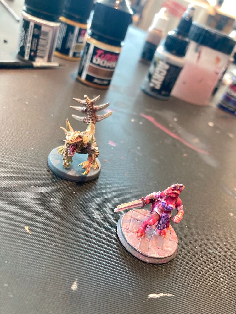 photo of 2 minis: 1 is a greenish gold lizard monster and the other is a red and purple lizard person with a sword.