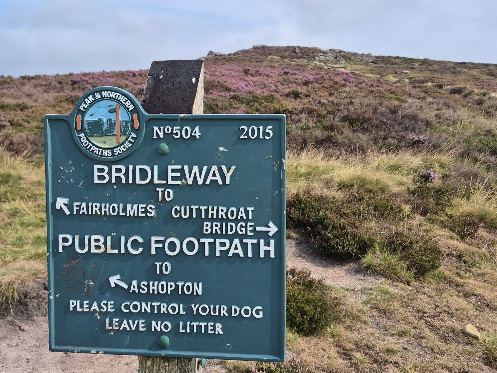 Peak District waymarker in front of heather moorland, one way pointing to Cutthroat Bridge