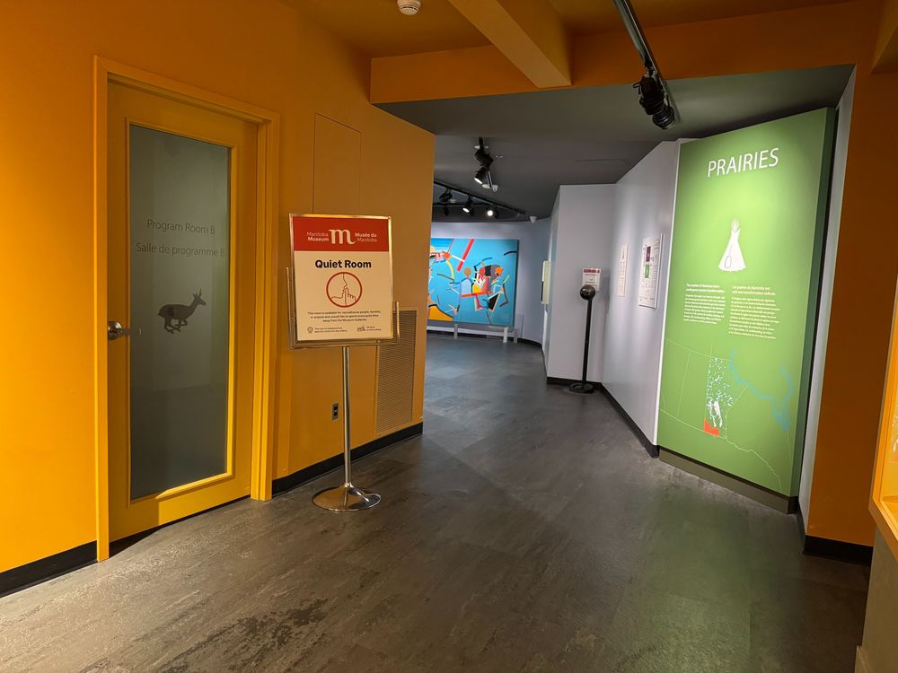 A hallway in the Museum Galleries with a frosted door leading to the Quiet Room on the left side, and the sign for the entrance to the Prairies Gallery on the right side.