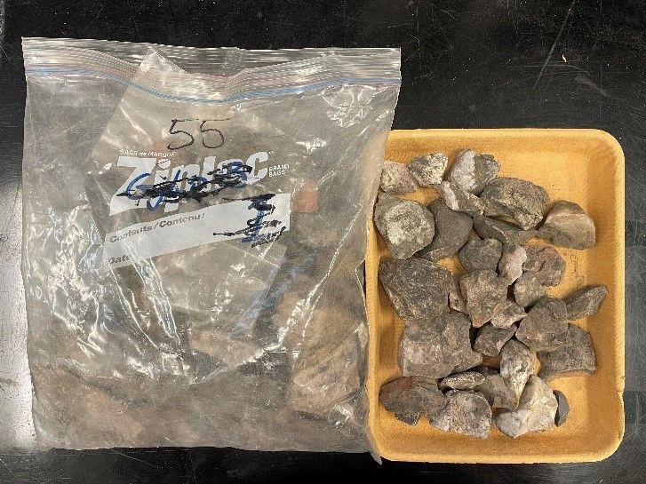 A large freezer bag labelled "55" filled with dirt and excavated artifacts next to a plastic tub containing more of the same.