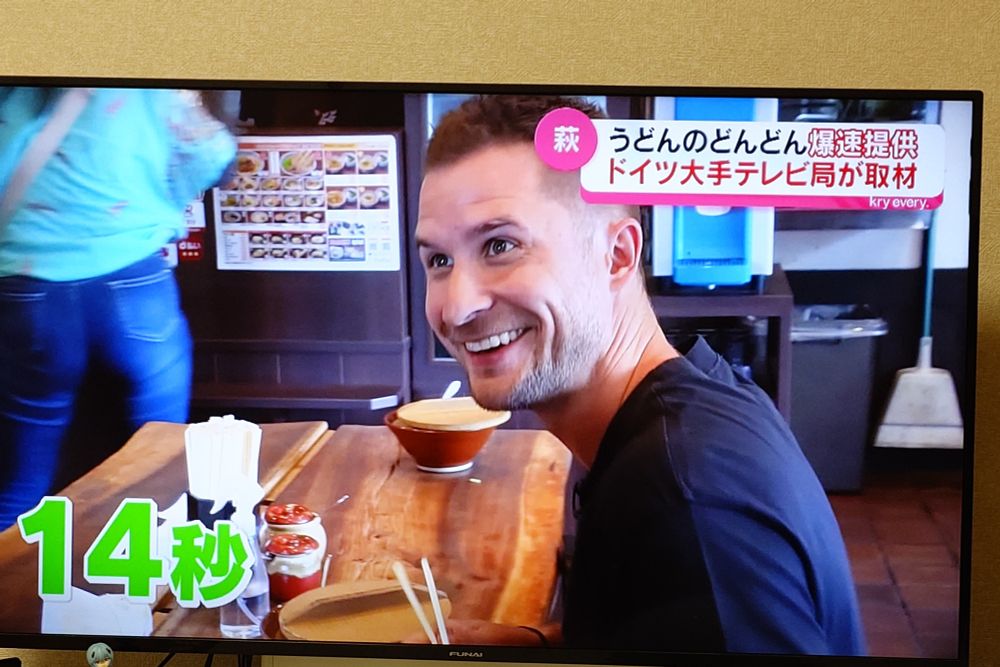 A shot of a crew making a tv program. A German food reporter is looking surprised as he looks at the camera. A caption in the corner says "14 seconds" in Japanese.
