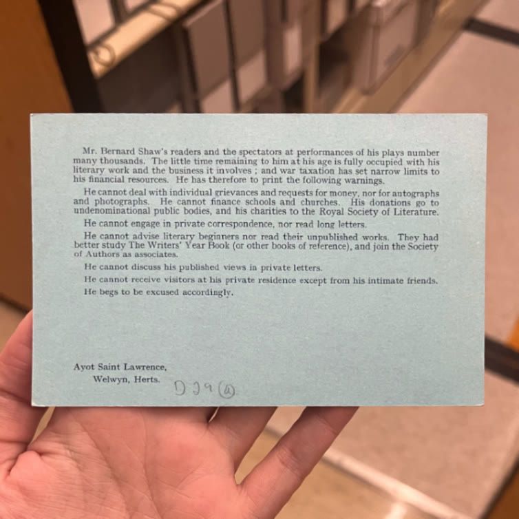 Postcard held in front of shelves of books. Text reads "Mr. Bernard Shaw's readers and spectators at performances of his plays number many thousands. The little time remaining to him at his age is fully occupied with his literary work and  and the business it involves; and war taxation has set narrow limits to his financial resources.  He has therefore to print the following warnings. He cannot deal with individual grievances and requests for money, nor for autographs and photographs..."