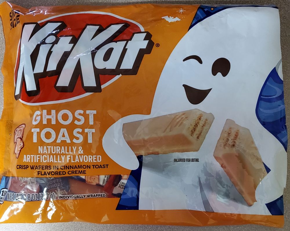 An bag of KitKat Ghost Toast flavored candy that has winking ghost against an orange background. It is breaking open a bar to expose the magical deliciousness inside.