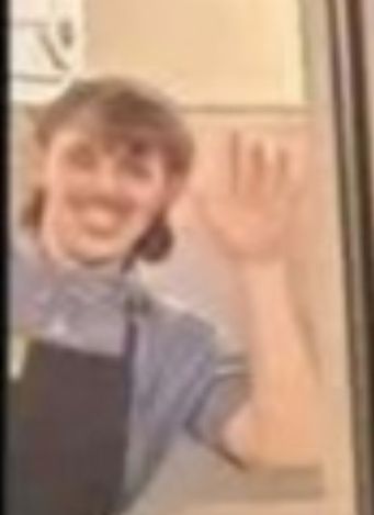 A fuzzy, zoomed in image of a Waffle House employee with what appears to be a mullet and mustache waving as part of him photo bombing another image. 