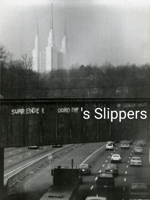 Black and white photo of the Mormon temple in the background and a bridge in the foreground that says "surrender Dorothy" with text added to say "surrender Dorothy's slippers"