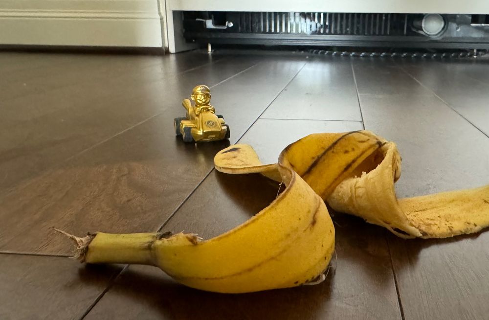 a mini golden mario rc car (from mario kart) appears to drive towards a relatively large banana peel sitting on the floor