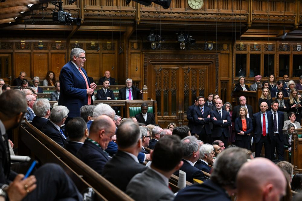 Gavin Robinson MP (Belfast East, Democratic Unionist Party) is standing in the middle rows of the benches, wearing a blue jacker and salmon tie. He is mid-speech and his hands are together in front of him.