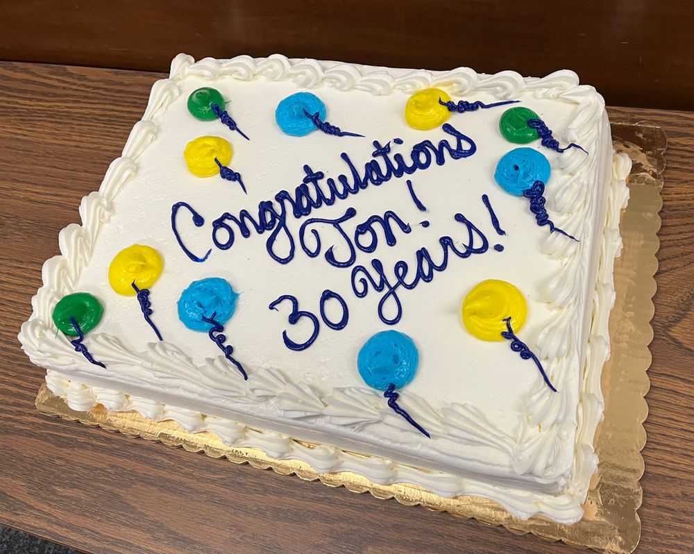 A yellow cake with heavy buttercream frosting with yellow, blue, and green frosting balloons, and Congratulations Jon 30 years! written on it.