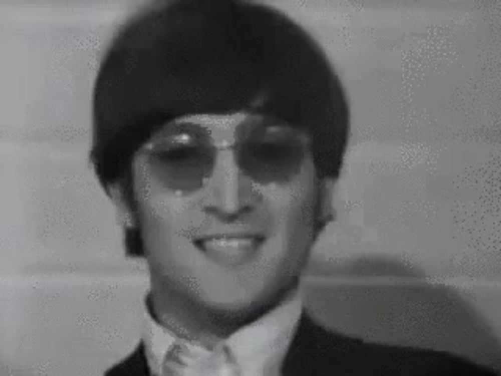 a black and white photo of john lennon wearing sunglasses and a suit and tie .