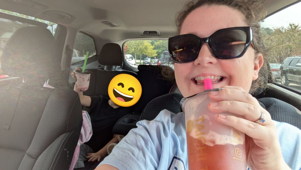 Julia smiling with a cup of bubble tea to her mouth in her car; her son with a 😄 emoji over his face is posing with his strawberry milk tea from the backseat.