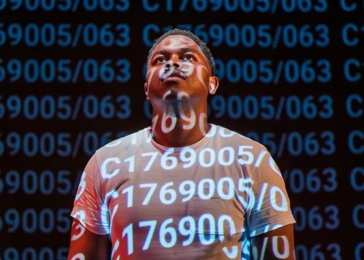 Close up of black man wearing white T-shirt looking up, with letters and numbers projected onto him