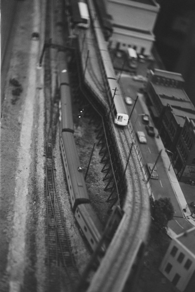 A B/W film photo of a model paspenger train passing below a viaduct with a legacy bart train on it

Canon 7
Rollei IR