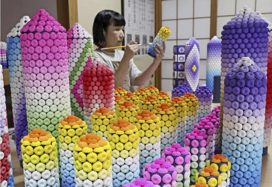 A worker attaches rakugan sweets to round pillars with conical tops. The rakugan are blue, mauve, red, orange yellow, green and white.