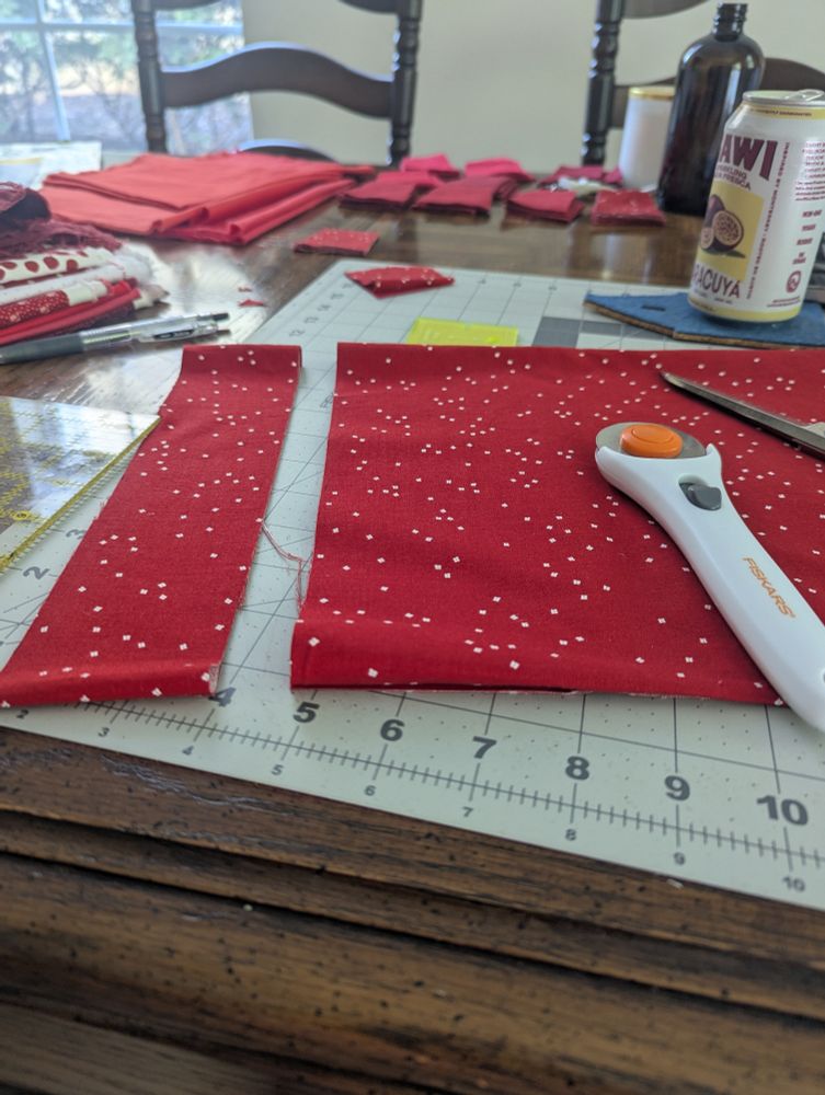 Table covered in quilting mats and cutting equipment, with piles of red and white fabric