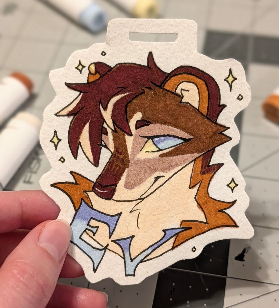 Picture of a badge for my marten fursona, Ev. It is a bust made with markers and pen on watercolor paper. Her head is tilted downward and she's softly smiling.
