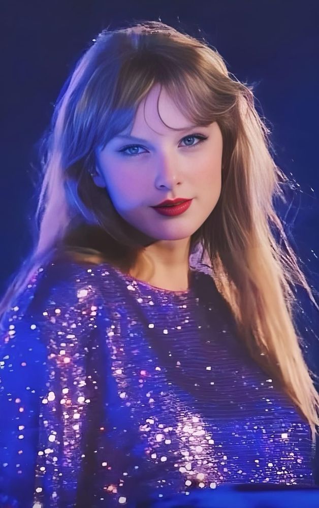 Taylor Swift staring at the camera while with her hair down, wearing a purple sequin dress and red lipstick