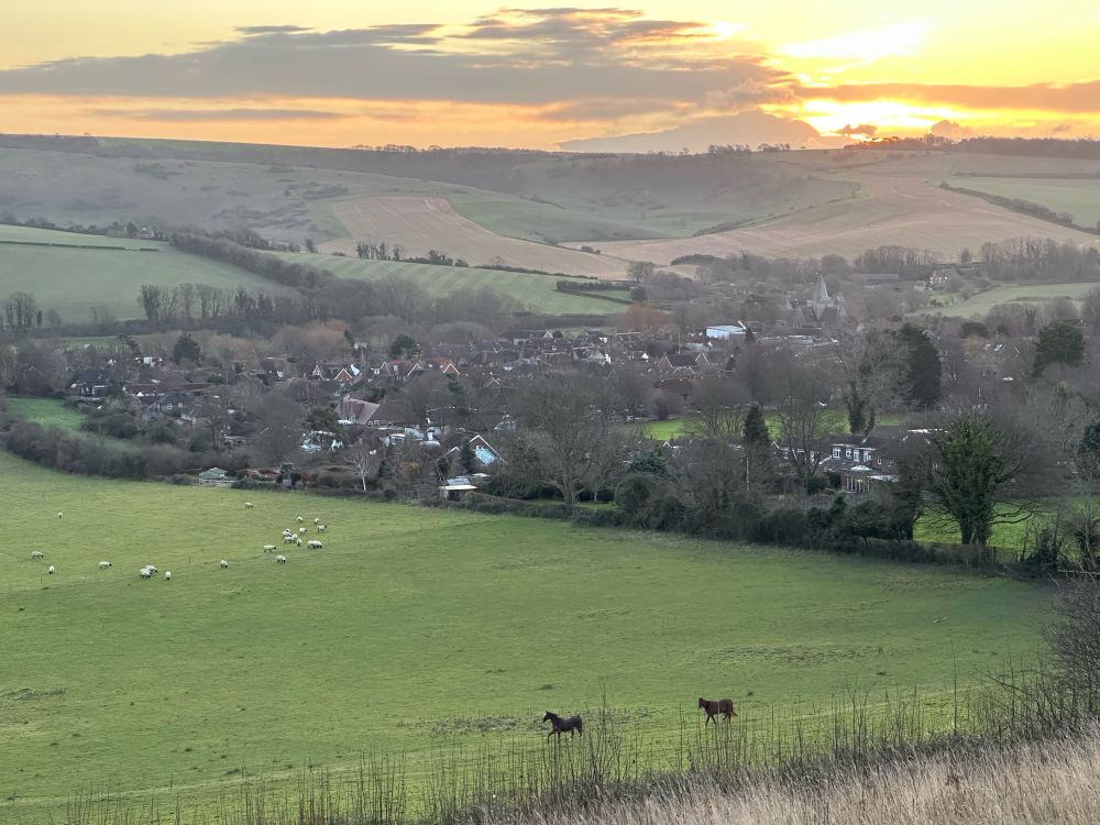 Sussex village at dawn with horses and sheep in the foreground and the South Downs in the background.