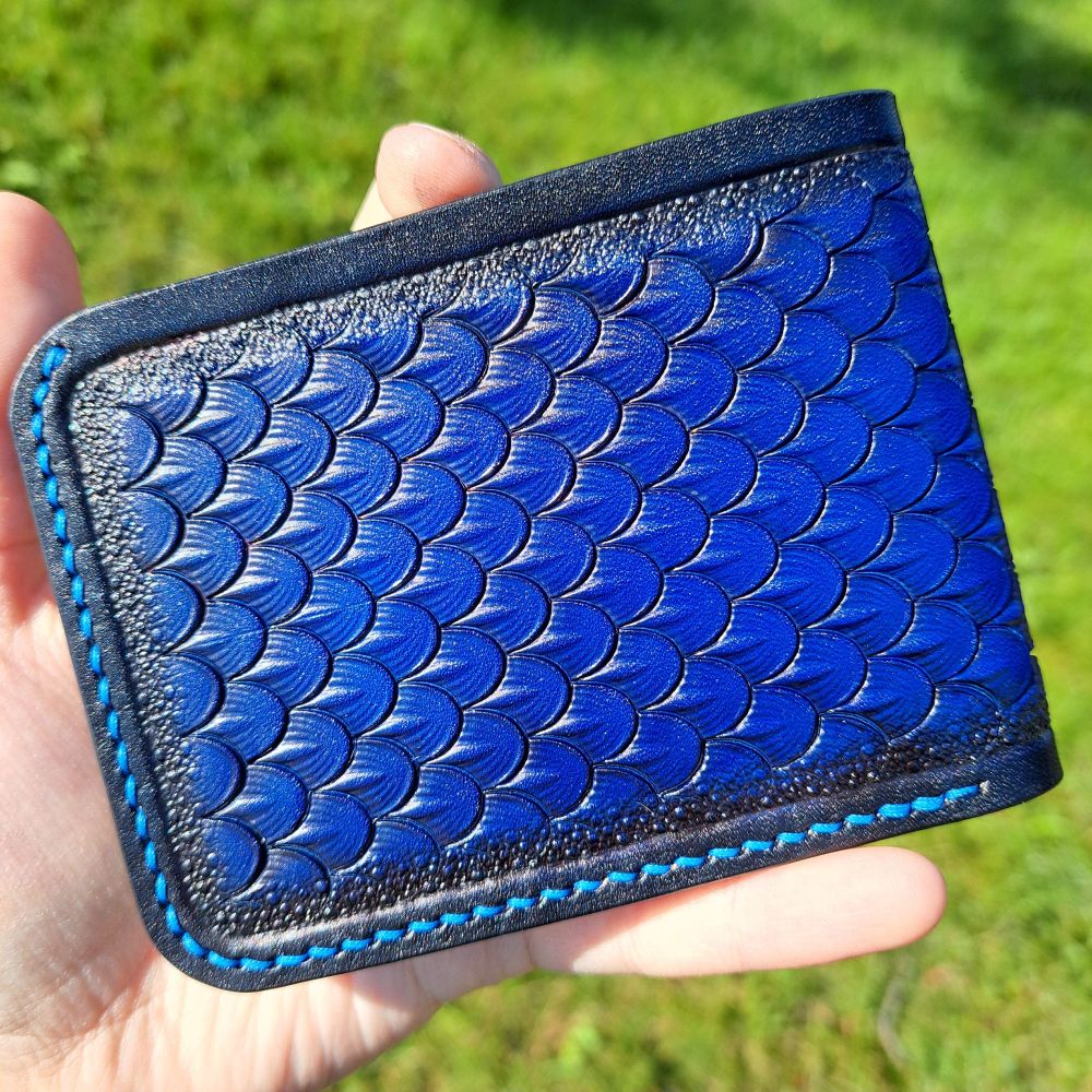 The back side of the folded wallet showing the dragon scales of this side.  It is the same as the first picture with cool blue scales that fade to smooth black edges. It also has matching thread. The scales run to the right.