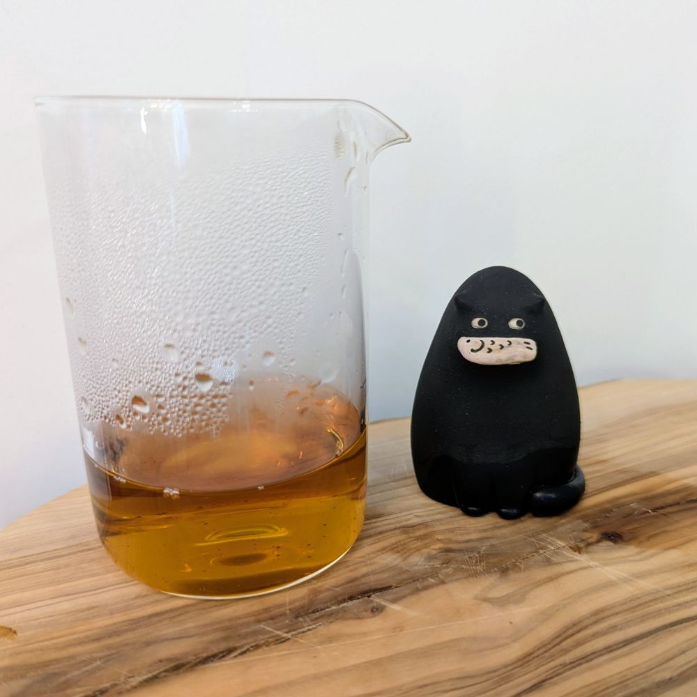Left: A glass gong dao bei sits with the brewed tea liquor. Right: A clay tea pet in the shape of a black cat holding a fish.