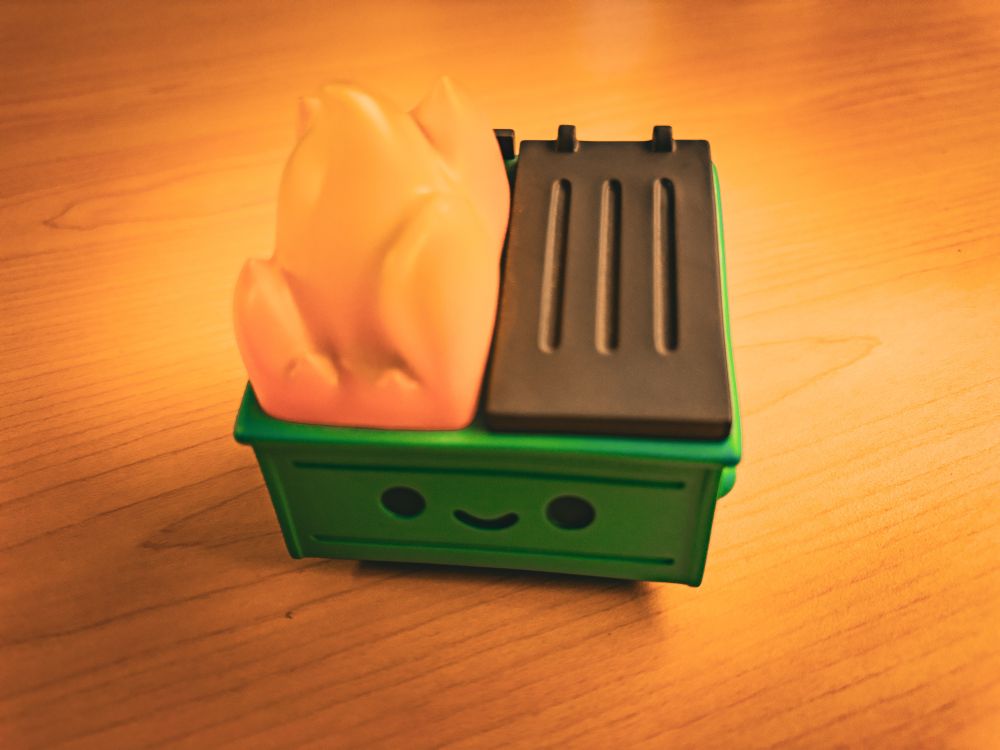 A dumpster fire toy with a cute smile sits on a wooden table