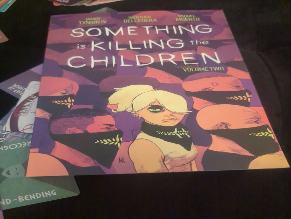 Cover of a graphic novel with a blond hero deadass staring you down with one eye, the other hidden by her bangs. Other masked people blur into the background, all facing right 