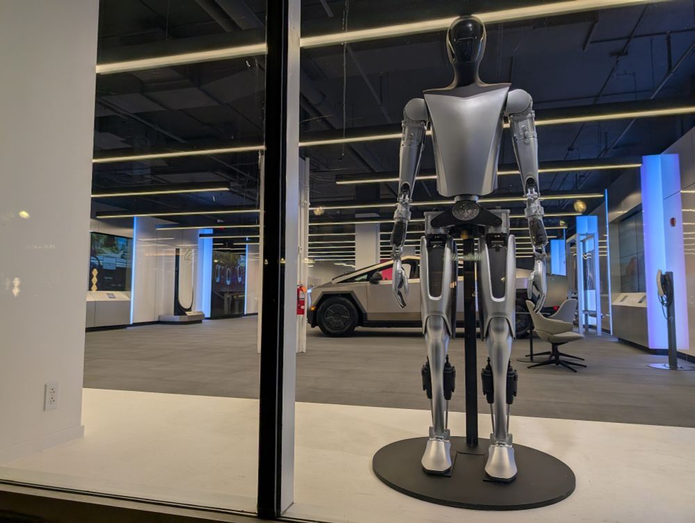 An Optimus robot (or maybe just an inert version of one) and a Cybertruck behind the glass of Tesla's outpost at 3307 M St. NW. 