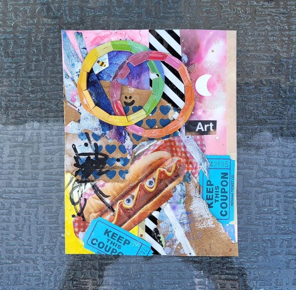 Photo of a very colorful mixed media analog collage sitting on a textured glass-topped table. Collage includes a rainbow, a hot dog with googly eyes affixed, old raffle tickets, scribbles, used cardboard scraps, misc small art pieces, and more.