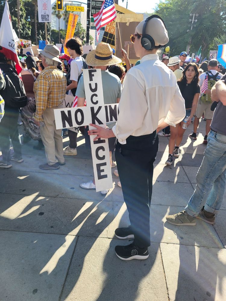 Woman dressed as the LA dancing Jesus guy. Cross says "Fuck Ice" and "No Kings"