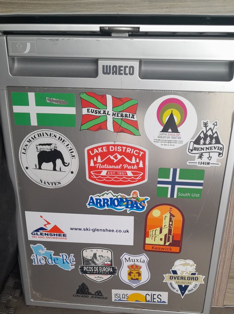 Travel stickers on a silver campervan fridge
