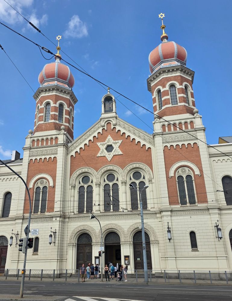 The front elevation, two towers surmounted with onion domes and then stars of david in gold surround a half Gothic, half Romanesque front with a huge star of david decoration.