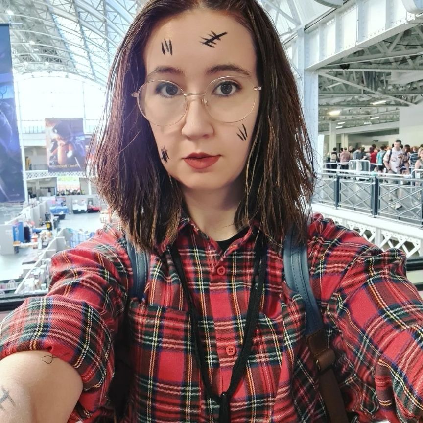 Selfie of a cosplayer dressed as Amy Pond. She is wearing a red plaid shirt, and has black tally marks all over her skin. 