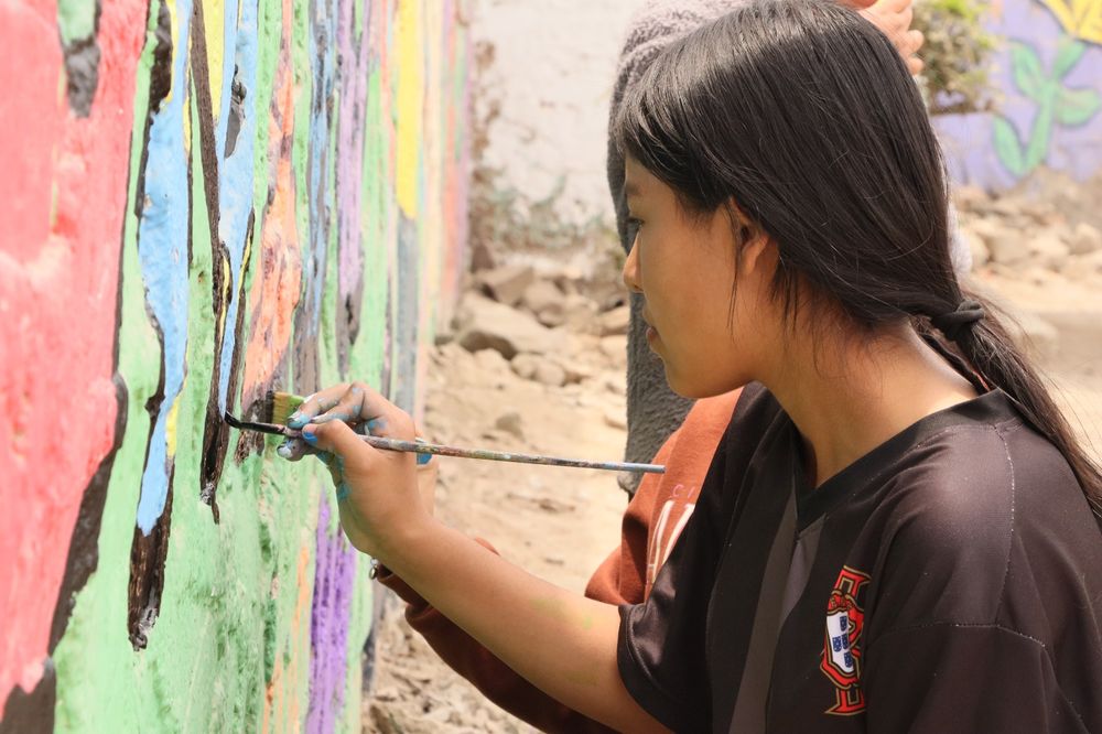 A photo showing a girl painting a mural on a wall. 