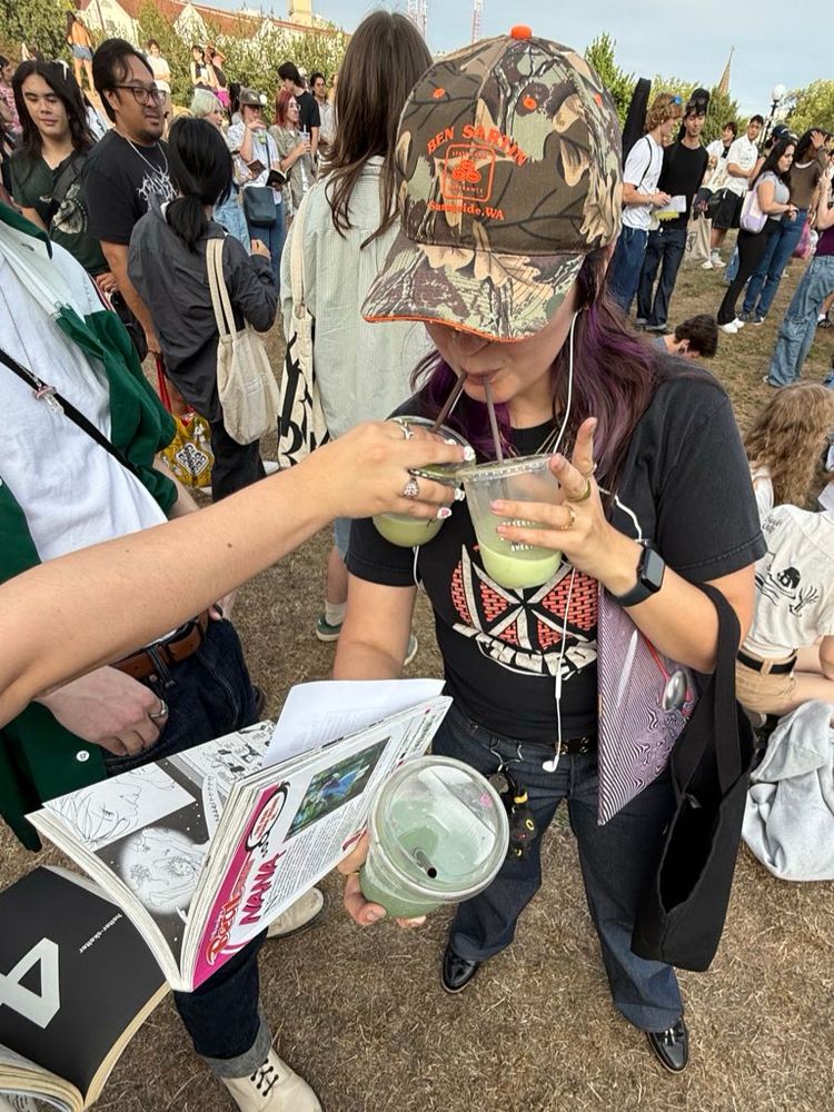 A nonbinary individual drinking two matchas while reading a page from the manga “Nana” while holding a third matcha.