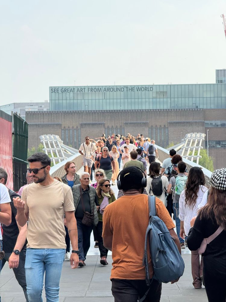 Photo of the Millennium Bridge on a sunny day with lots of people crossing.