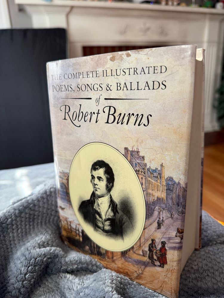 A vintage book of "The Complete Illustrated Poems, Songs & Ballads of Robert Burns" with an illustration of Edinburgh architecture on the cover and a portrait in an oval frame. The book appears to be a collector's or special edition, with its aged, classic design and historical illustration style.