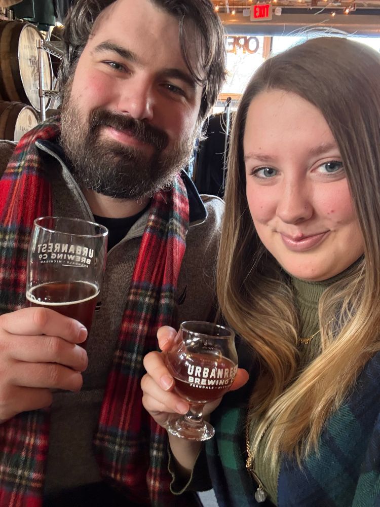  A photo taken at Urban Rest Brewing Co., showing a man and a woman enjoying some craft beers.They're both dressed for the occasion, each wearing tartan scarves, adding to the Scottish theme of their outing.