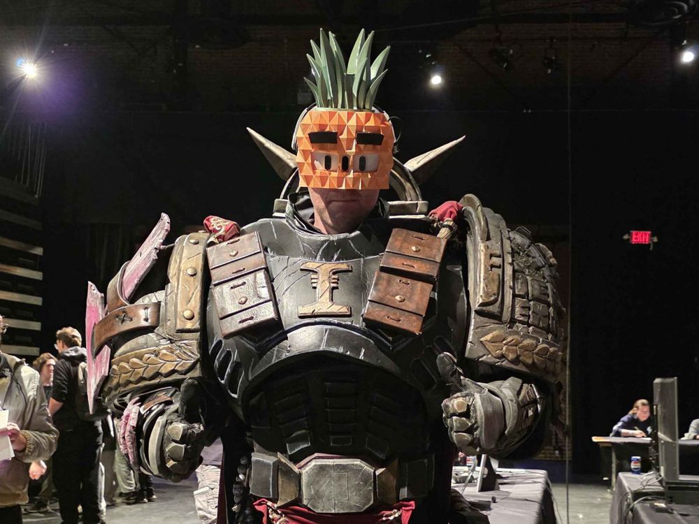 A person cosplaying as a giant space marine wearing a pineapple mask. They are giving a thumbs up.