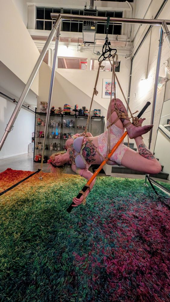 Lain tied to an orange stick in a side suspension 