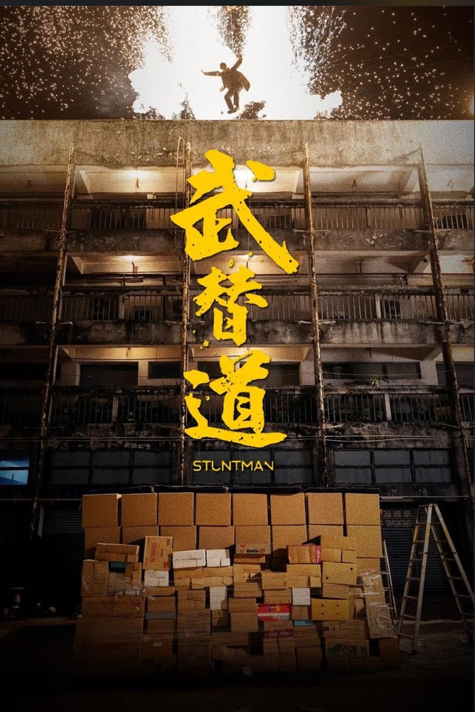 Affiche de Stuntman d’Albert & Herbert Leung. Un homme est en train de sauter d’un immeuble sur une pile de cartons en guise de matelas. Derrière lui, une explosion.