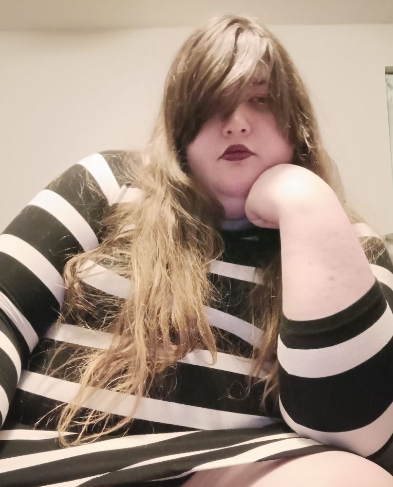 olus size woman in a black and white striped dress and black lipstick resting her chin on her hand