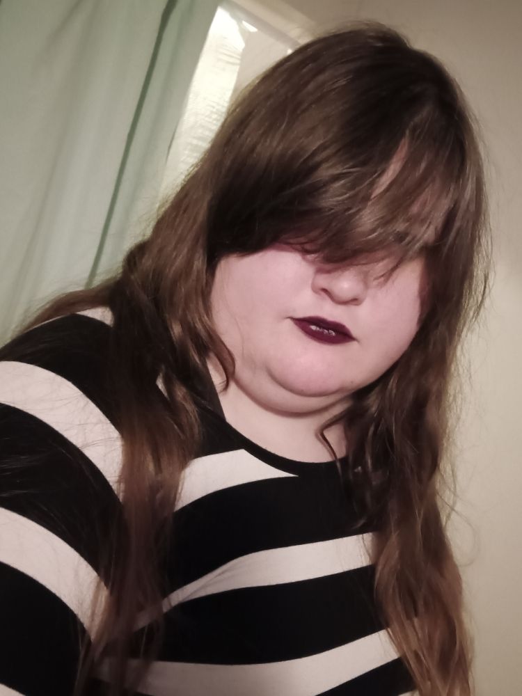 plus size woman in a black and white striped dress with long brown hair and black lipstick, her bangs obscure her eyes