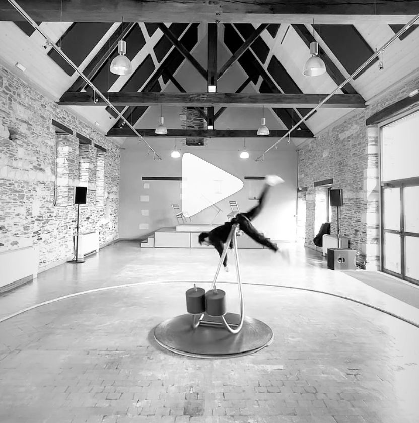 Bastien Dausse's device that allows the dancer to appear to defy gravity. The mechanism is curved, like the Nike swoosh, resting on the lowest point. The short end is loaded with weights and the longer end is attached to the dancer's waist. When the dancer pushes up, the device rocks on the low point, lifting them up to a meter off the ground and letting them fall softly back to Earth.