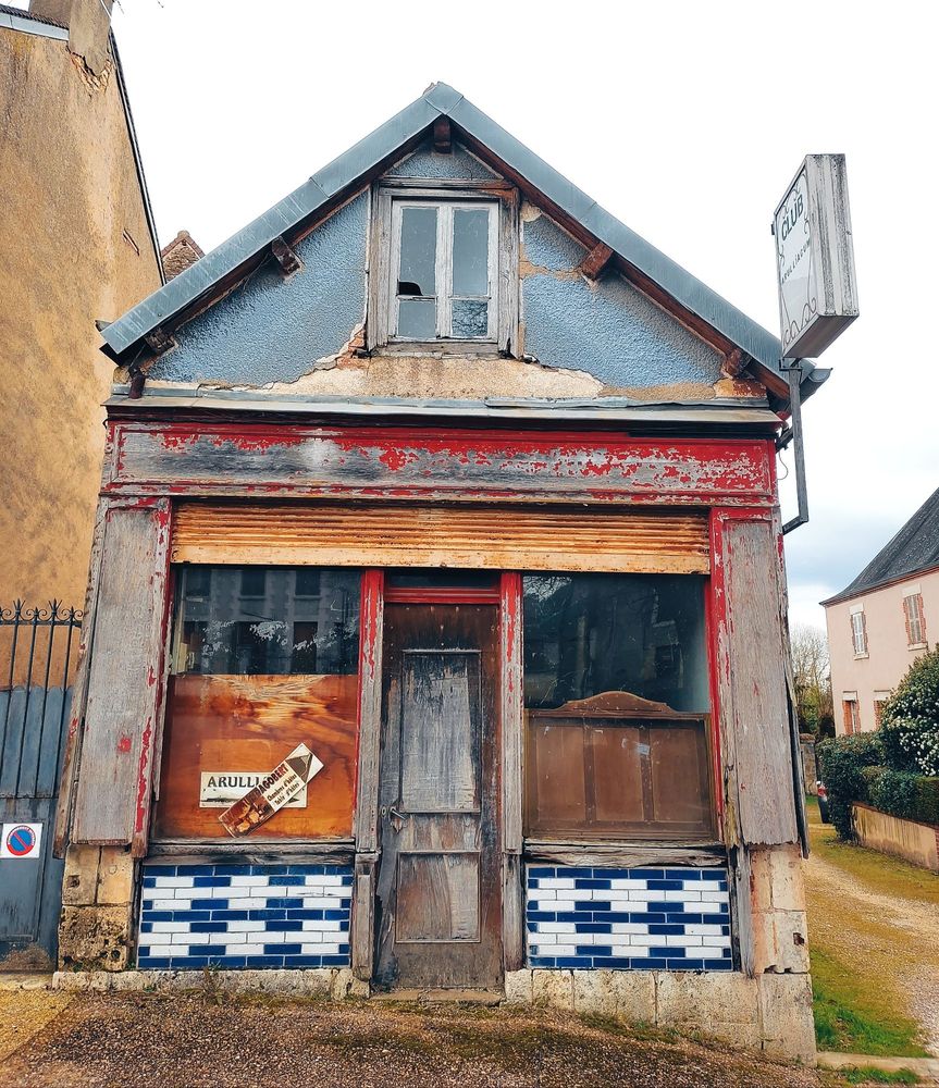 Vitrine désaffectée d'un petit commerce avec de jolies tuiles céramiques bleues et blanches sous les fenêtres et des panneaux de bois avec traces de peintures rouge 