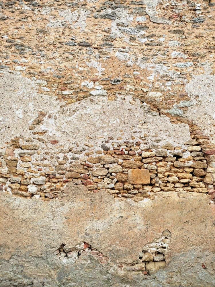 Mur de pierre avec enduit partiellement disparu, révélant de belles pierres jaunes