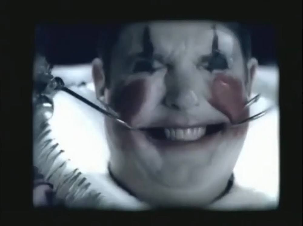A screenshot from this commercial for Universal's Halloween Horror Nights in 2003: https://youtu.be/RmwTcJi9Uwo?si=duedQVX2x21YvOmZ

A clown's mouth is being forced in to a smile with hooks.